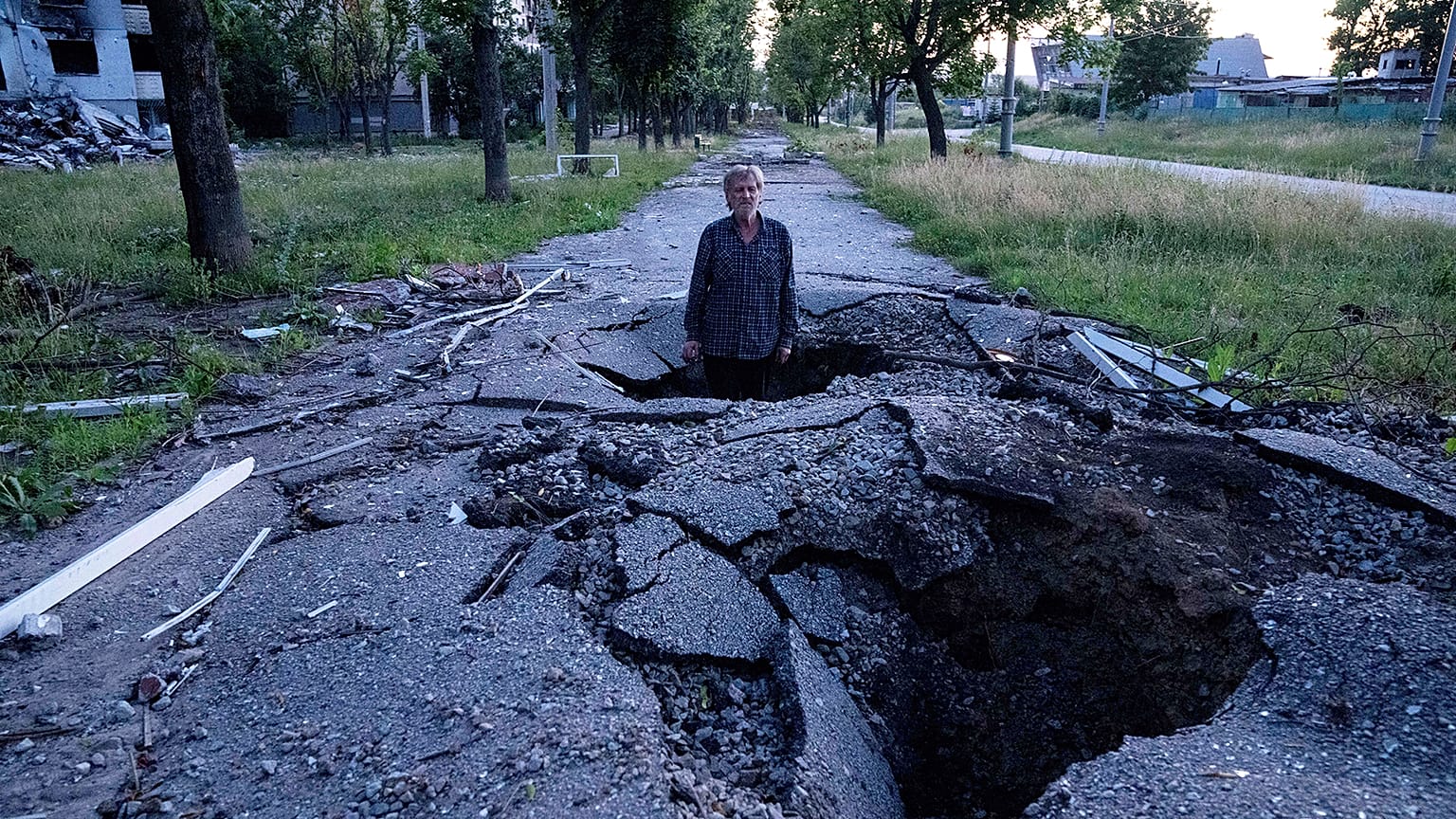 Viktor Shevchenko stands in a crater to show its depth after a Russian attack in the Saltivka district in Kharkiv, 1 July 2022
