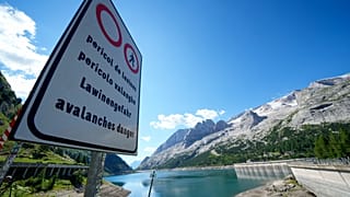 A signpost reading "avalanche danger" is seen in front of the Marmolada mountain and the Punta Rocca glacier near Canazei, in the Italian Alps in northern Italy, July 6, 2022.