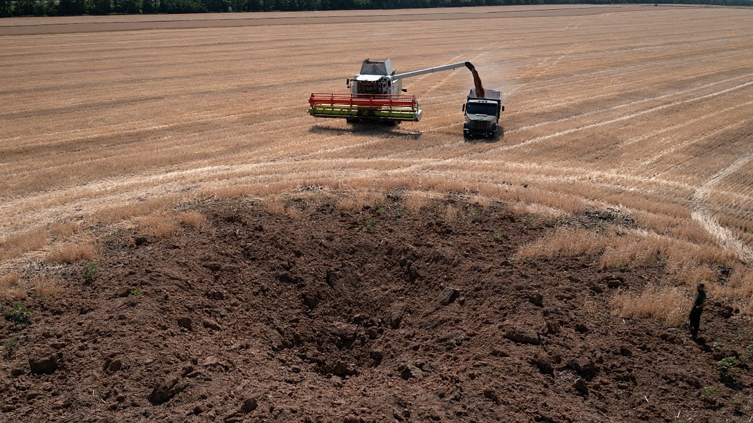 A crater left by a Russian rocket attack is seen as a farmer collects harvest in a field that is ten kilometres away from the frontline, July 4, 2022.