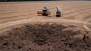 A crater left by a Russian rocket attack is seen as a farmer collects harvest in a field that is ten kilometres away from the frontline, July 4, 2022.