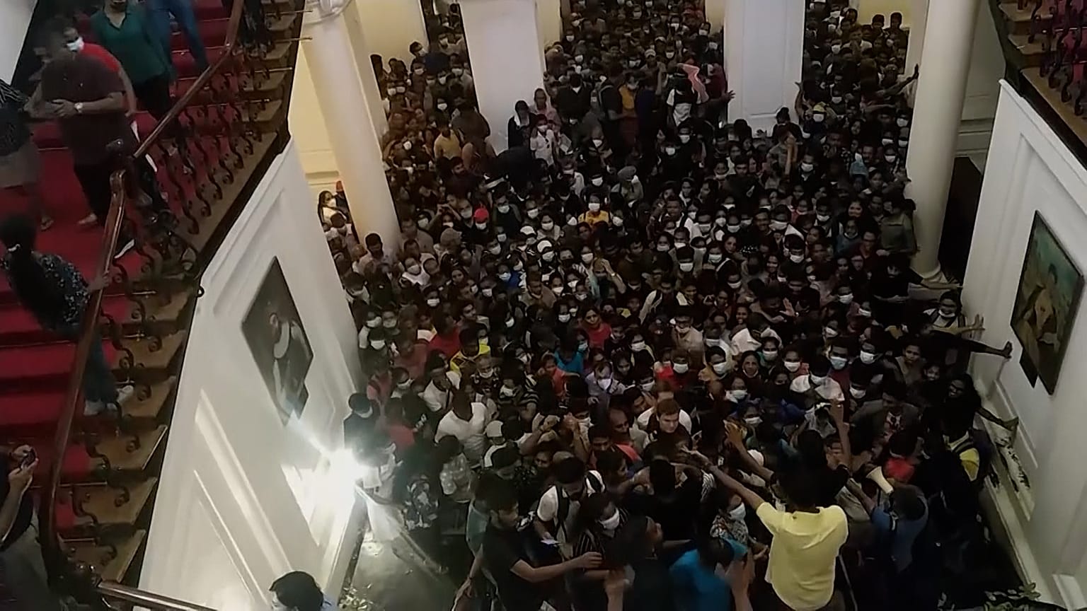 Crowds of people inside Sri Lankan presidential palace, walking up stairs.