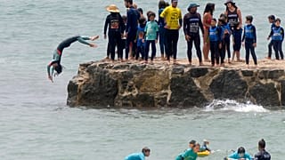 Egy fiatal szörfős ugrik a vízbe Lisszabon Carcavelos strandjánál