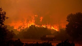 Un camión que transporta tanques con agua pasa junto a un incendio forestal cerca de Ansiao, en el centro de Portugal, el miércoles 13 de julio de 2022.