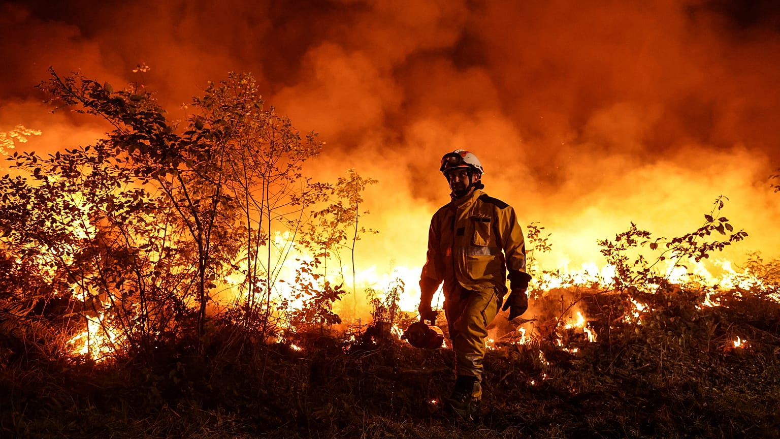Tactical firefighters (wearing yellow gear) set a backfire to a plot of land to prevent the wildfire from spreading in Louchats, south-western France, on July 17, 2022.