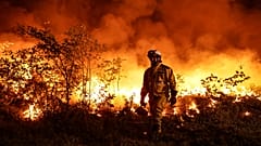 Tactical firefighters (wearing yellow gear) set a backfire to a plot of land to prevent the wildfire from spreading in Louchats, south-western France, on July 17, 2022.