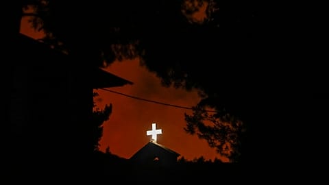Das weiße Kreuz einer Kirche in Penteli, nordöstlich von Athen, vor einem Flammenmeer, 19.07.2022