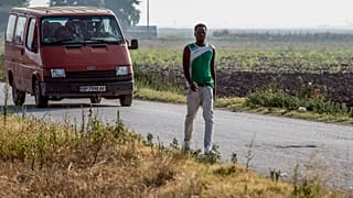 Migrant workers travel in a mini-bus as others take part in a march near Foggia on August 8, 2018.