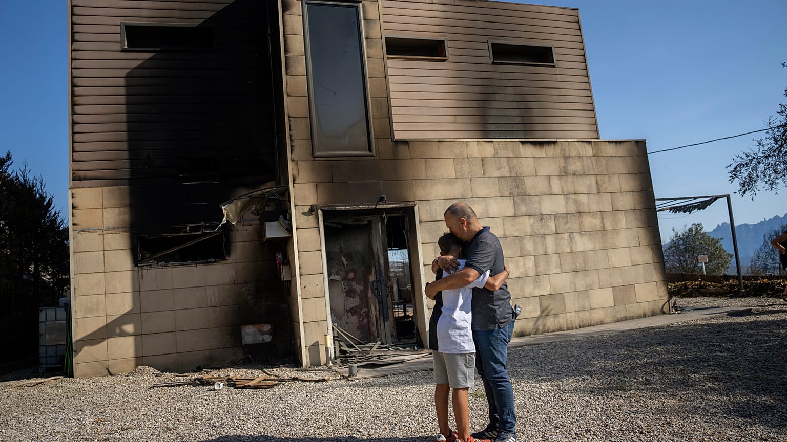 Alex Codonyer abraza a su hijo Alan junto a su casa quemada durante un incendio forestal cerca de la localidad de El Pont de Vilomara, España, el 19 de julio de 2022.