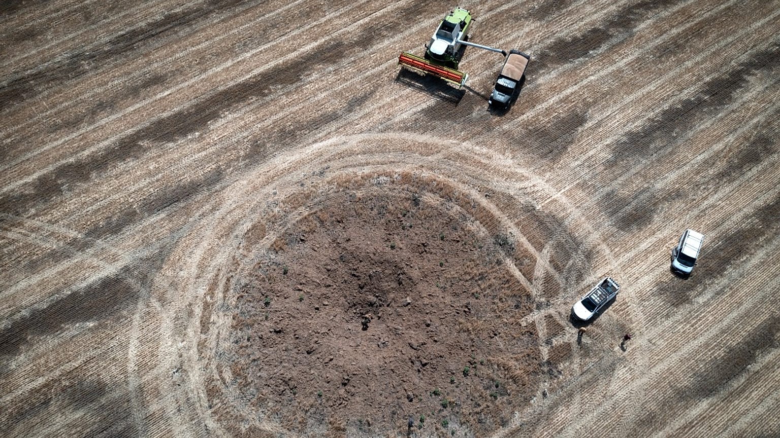 Un agriculteur en train de récolter son champ autour d'un cratère formé par une roquette russe, dans la région de Dnipropetrovsk, en Ukraine, le 4 juillet 2022.