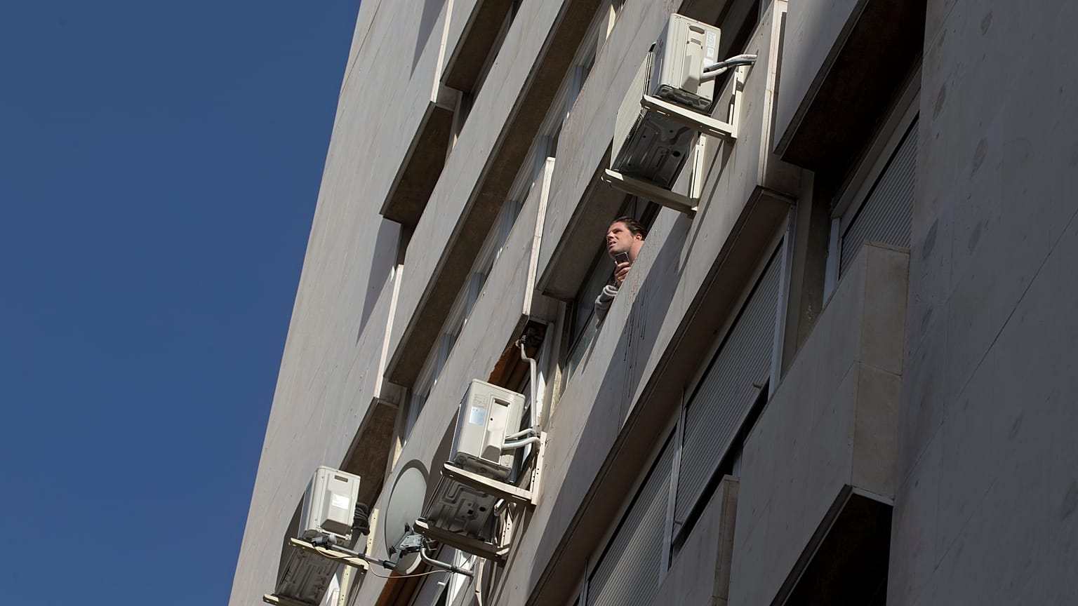 A man looks out of a window in a housing block with air conditioning units on the outside in Madrid, Spain, Tuesday, Sept. 6, 2016. 