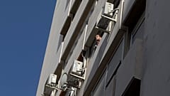 A man looks out of a window in a housing block with air conditioning units on the outside in Madrid, Spain, Tuesday, Sept. 6, 2016. 