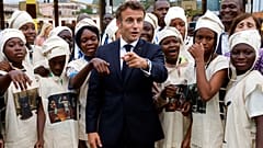 Macron poses with young women in traditional costumes as they celebrate the Abomey Treasures, during his visit to the French College in Benin, 27 July 2022. 