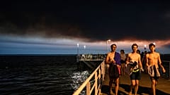 Swimmers walk on the Le Moulleau pier in Arcachon, southwestern France Monday July 18, 2022, as a large cloud of black smoke laden with ashes coming from a giant wildfire.