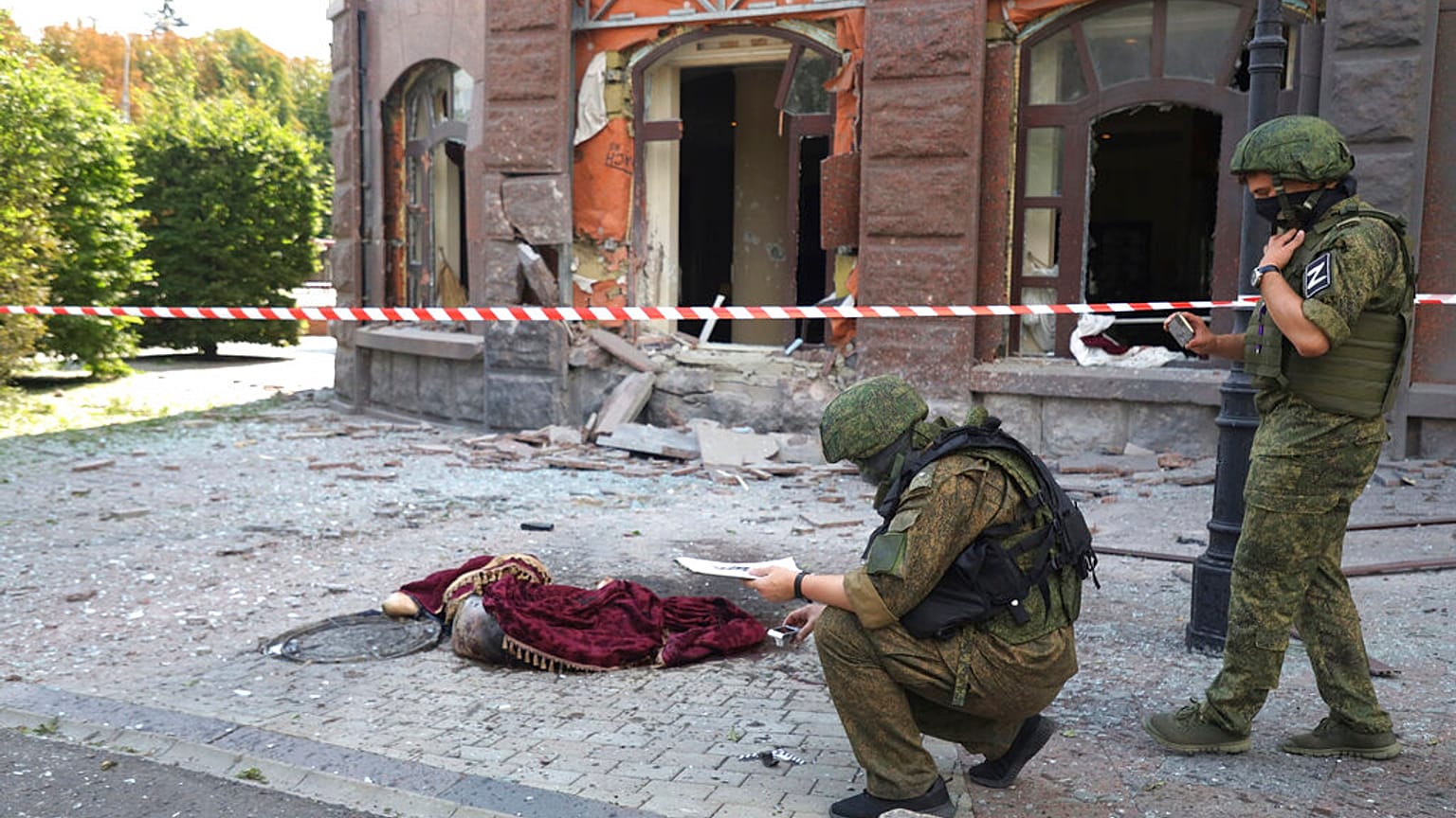 Agentes da comissão de investigação inspecionam uma área bombardeada onde jaz um corpo sem vida coberto, na região separatista de Donetsk, Ucrânia