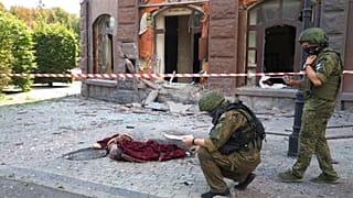 Agentes da comissão de investigação inspecionam uma área bombardeada onde jaz um corpo sem vida coberto, na região separatista de Donetsk, Ucrânia