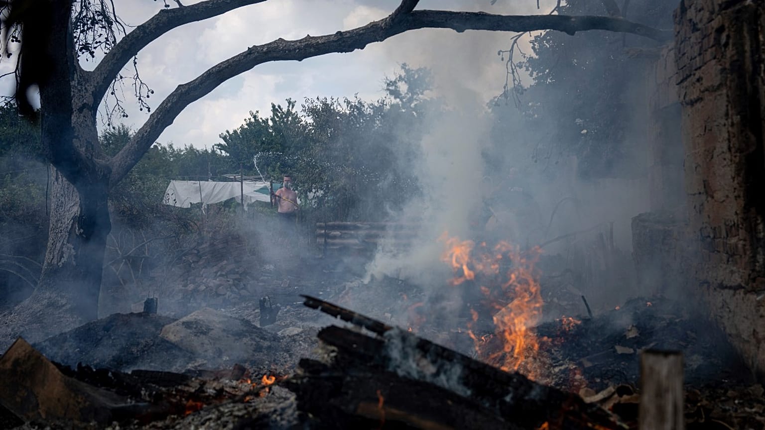 A local resident, back, tries to stop the fire at a neighbor's house destroyed by a Russian attack in Mykolaiv, Ukraine, Friday, Aug. 5, 2022.