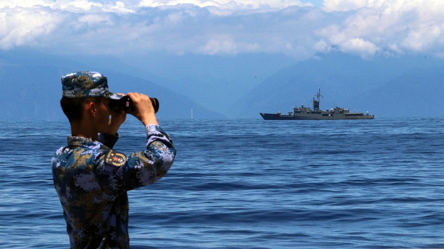 A People's Liberation Army member looks through binoculars during military exercises as Taiwan’s frigate Lan Yang is seen at the rear, on Friday, Aug. 5, 2022.