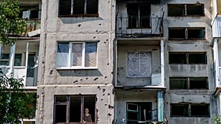 Пожилая женщина выглядывает из окна своей квартиры в Славянске после ночного обстрела (7 августа 2022 г.)