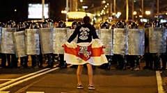 A protester holding an historical Belarusian flag stands in front of police officers as they block a road in Minsk , 9 August 2020