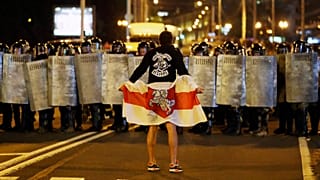 A protester holding an historical Belarusian flag stands in front of police officers as they block a road in Minsk , 9 August 2020