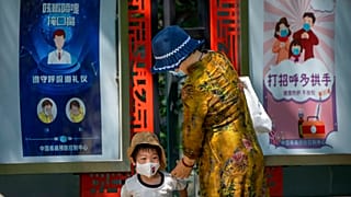 Egy nő és egy kisfiú Pekingben, maszkviselésre felszólító plakátok előtt - KÉPÜNK ILLUSZTRÁCIÓ