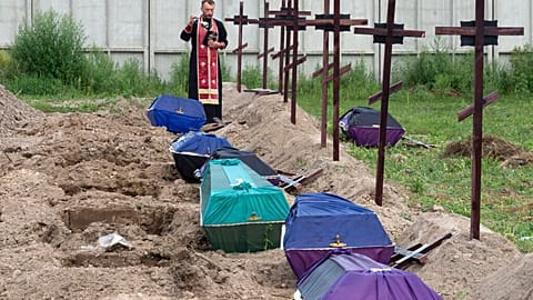 A priest prays for unidentified civilians allegedly killed by Russian troops during their occupation in Bucha, on the outskirts of Kyiv, Ukraine, Thursday, 11 Aug., 2022.