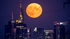 The full moon rises behind the buildings of the banking district in Frankfurt, Germany, Thursday, August 11, 2022. 