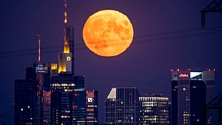 The full moon rises behind the buildings of the banking district in Frankfurt, Germany, Thursday, August 11, 2022. 