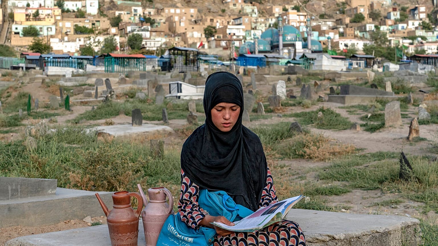 سارا، ۱۴ ساله، کتاب به دست در قبرستان کابل آب می‌فروشد، تابستان ۲۰۲۲ میلادی