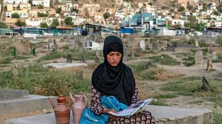 سارا، ۱۴ ساله، کتاب به دست در قبرستان کابل آب می‌فروشد، تابستان ۲۰۲۲ میلادی
