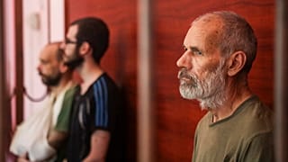 De g. à dr. : les Britanniques Andrew Hill, Dylan Healy et John Harding derrière les barreaux dans une salle d'audience à Donetsk, à l'est de l'Ukraine, le 15/08/2022