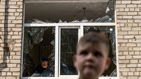A worker cleans up inside as Tikhon Pavlov, 11, walks past the Kramatorsk College of Technologies and Design after a rocket attack in the city. 