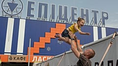 An escapee from the vicinity of the Zaporizhzhia nuclear power plant entertains his daughter below a sign that says "Epicentre", August 2022
