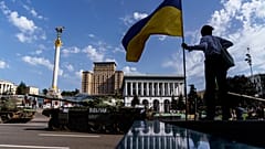 Eine Frau posiert mit Nationalflagge vor zerstörten russischen Panzern in Kiew.
