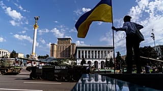 Eine Frau posiert mit Nationalflagge vor zerstörten russischen Panzern in Kiew.