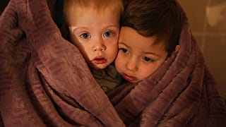 The children of medical workers warm themselves in a blanket as they wait for their relatives in a hospital in Mariupol, Ukraine, Friday, 4 March, 2022