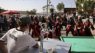 زائر يشاهد عرض راقصين فلسطينيين خلال مهرجان أكتوبر السنوي للبيرة في قرية طيبة في الضفة الغربية المحتلة. 2022/09/02