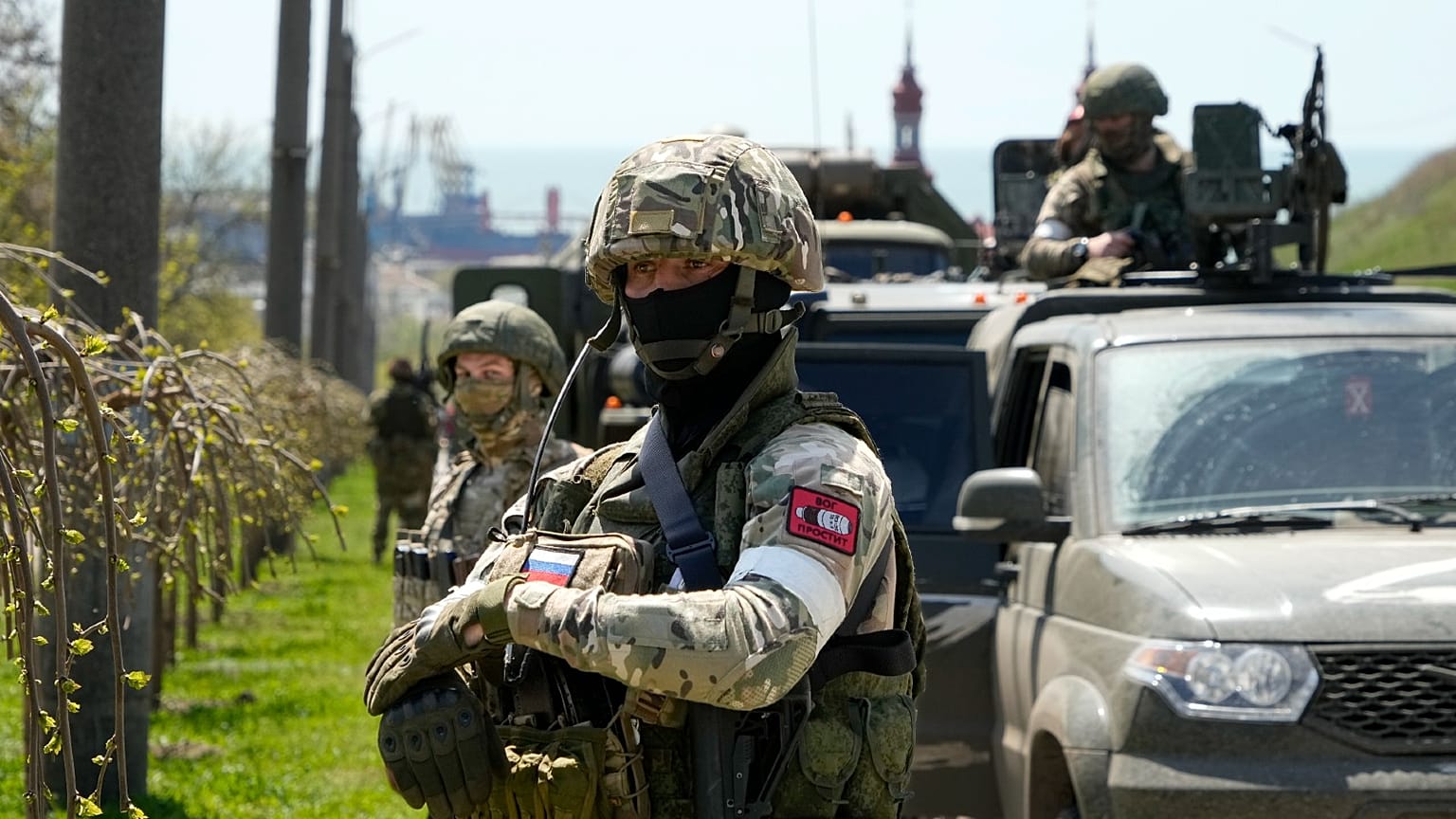 Russian servicemen stand near their military vehicles in Berdiansk with the Azov Sea in the background,