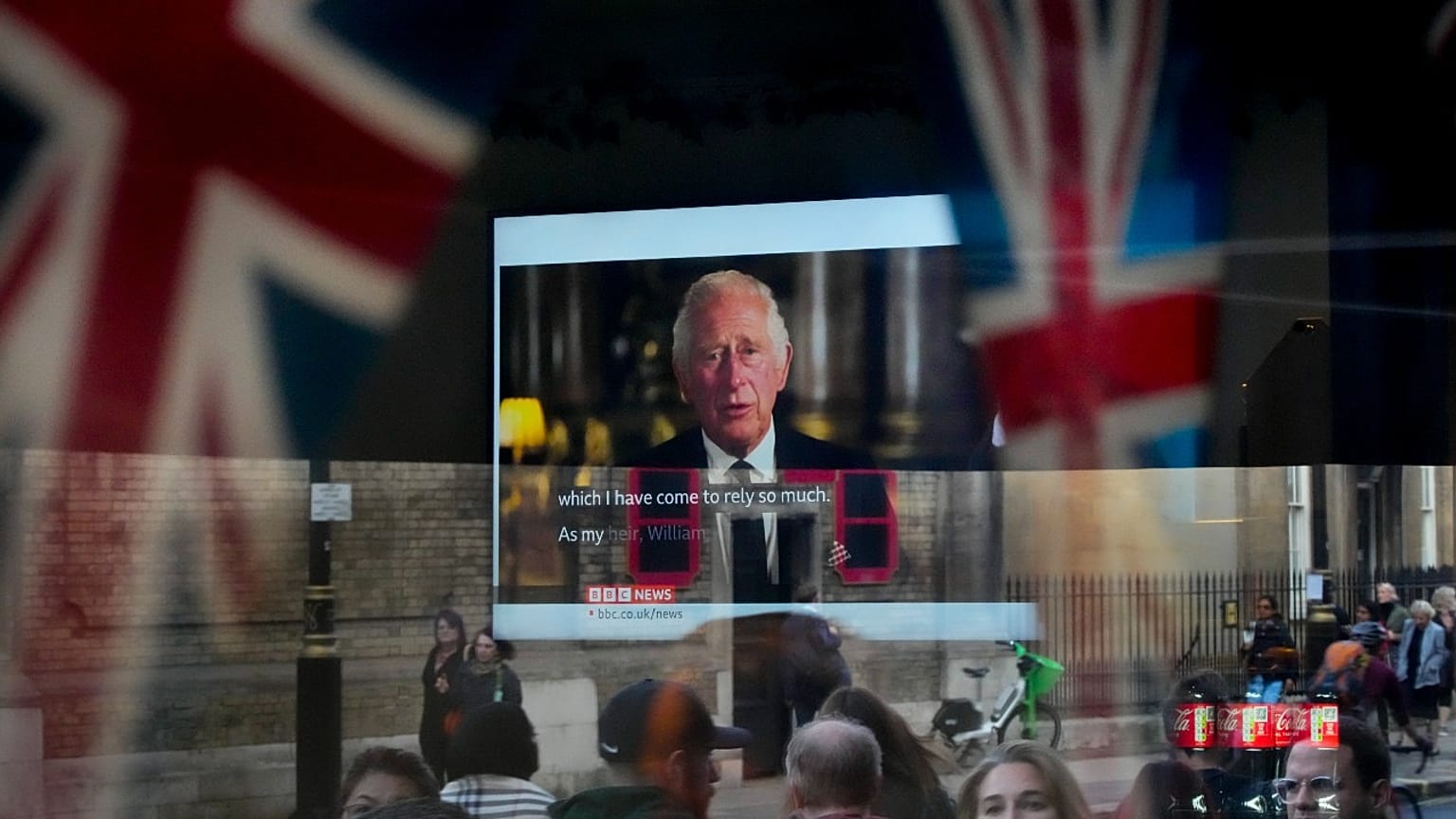 A passer-by tries to catch a glimpse of the televised speech of the new King Charles III as she passes by a pub in London, Friday, Sept. 9, 2022. 