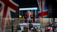 A passer-by tries to catch a glimpse of the televised speech of the new King Charles III as she passes by a pub in London, Friday, Sept. 9, 2022. 