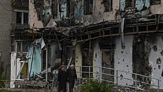 Casal em frente a edifício destruído em Izyum