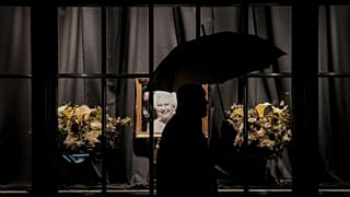 A man walks by a portrait of Queen Elizabeth II during a rainfall in central London, Tuesday, Sept. 13, 2022