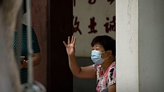 A woman wearing a face mask waves to a person at a public park in Beijing, Tuesday, Sept. 13, 2022. 