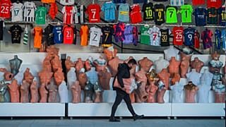 A shop clerk carries mannequins at a soccer jerseys stand at a tourist shopping area, in Belek, 12 March 2022