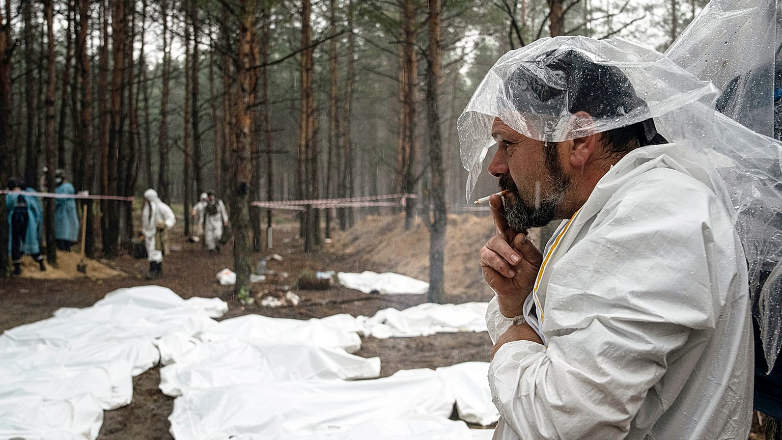 Expert smokes under the rain during the exhumation of bodies in the recently retaken area of Izium, 16 September 2022