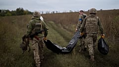 Ukrainian servicemen carry a bag containing the body of a Ukrainian soldier, centre, and a Russian soldier's remains, right. Saturday, 17 September 2022.