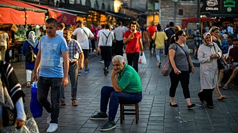 A man sits as people walk past by at the Egyptian spices market in Istanbul, Turkey, Thursday, Aug. 18, 2022.