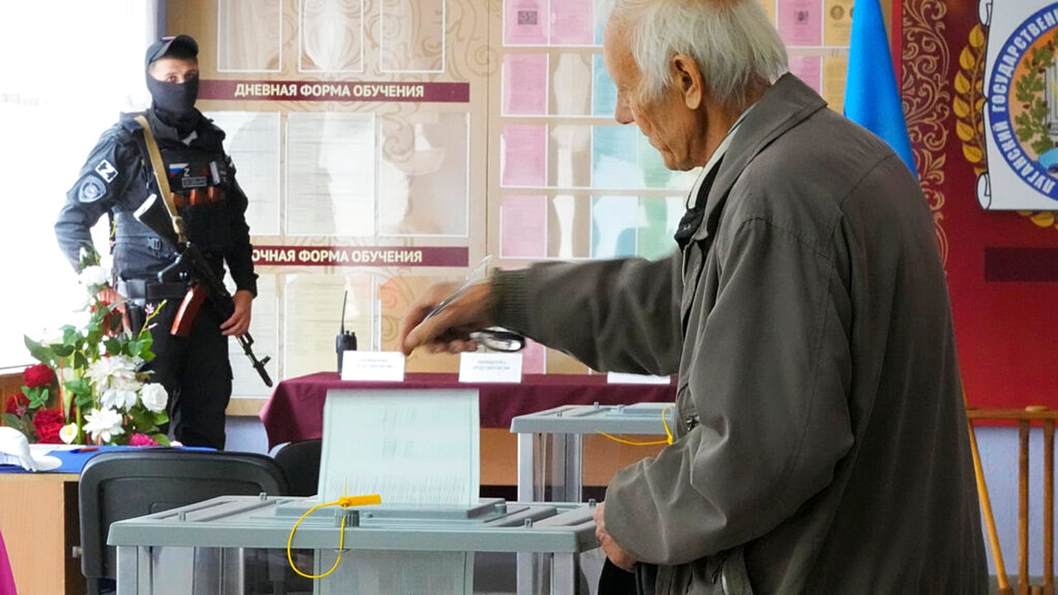 Un hombre acude a votar frente a un hombre armado en un colegio electoral.