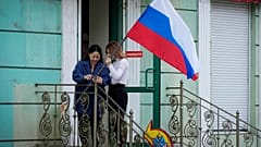 Zwei Frauen in  Luhansk befestigen eine russische Flagge an einem Treppengeländer