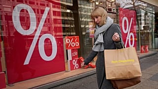 A woman walks with purchases past a store in Berlin, April 1, 2022. 